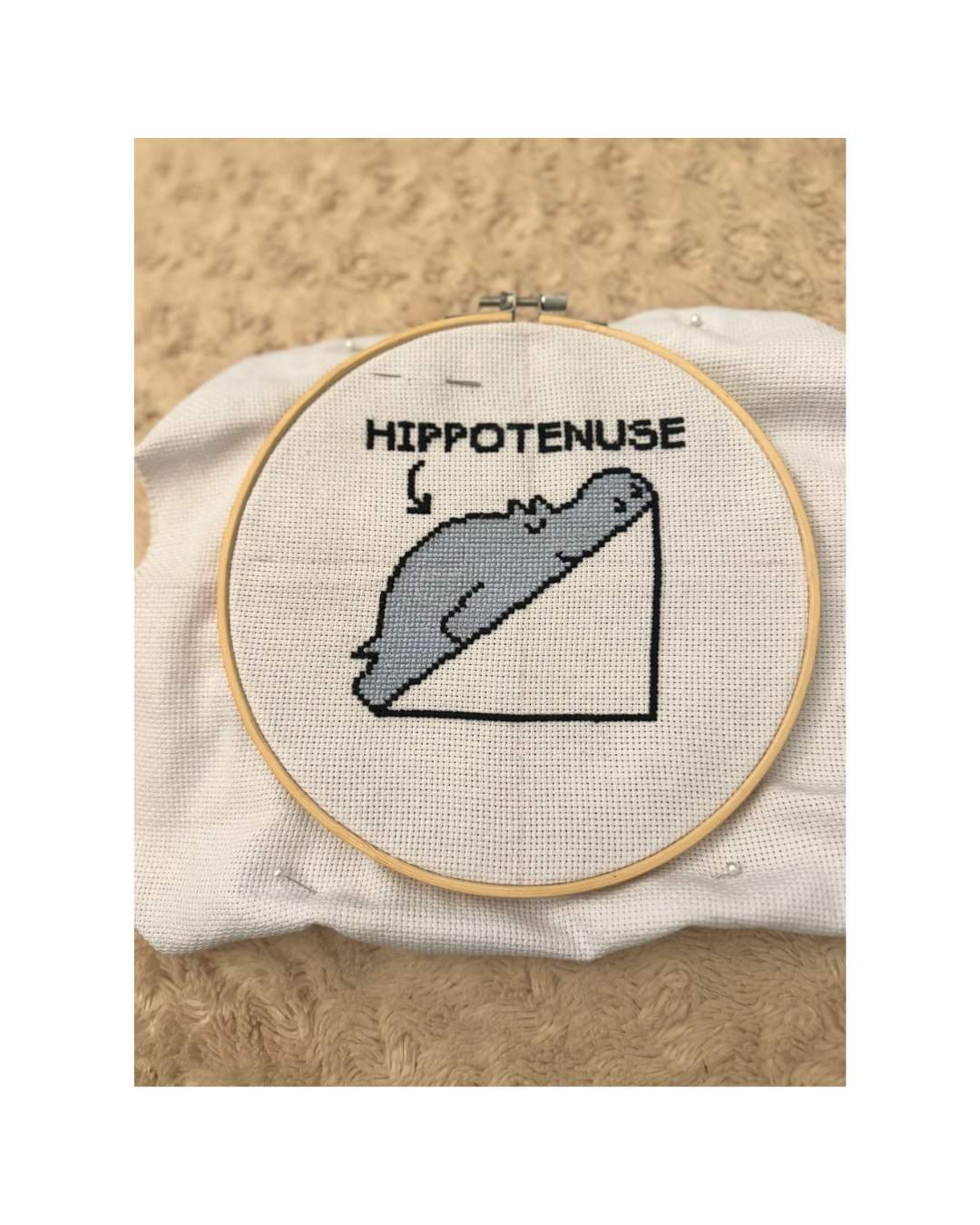 An embroidery hoop holds a stitched gray hippo along the hypotenuse of a triangle, below the word HIPPOTENUSE.