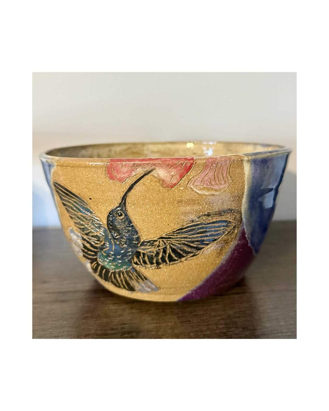 A glazed pottery bowl decorated with a hummingbird reaching toward a red flower.
